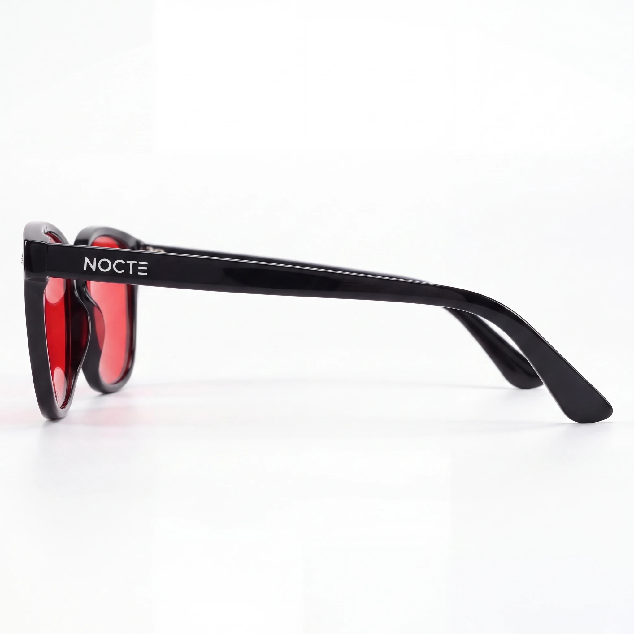 Perfil de la montura negra NOCTE, logo lateral y patilla curva; referencia fotografiada con cristal rojo